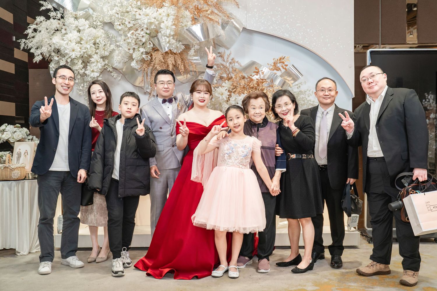 A group in formal attire poses together at an elegant event with floral decorations and a modern interior backdrop.
