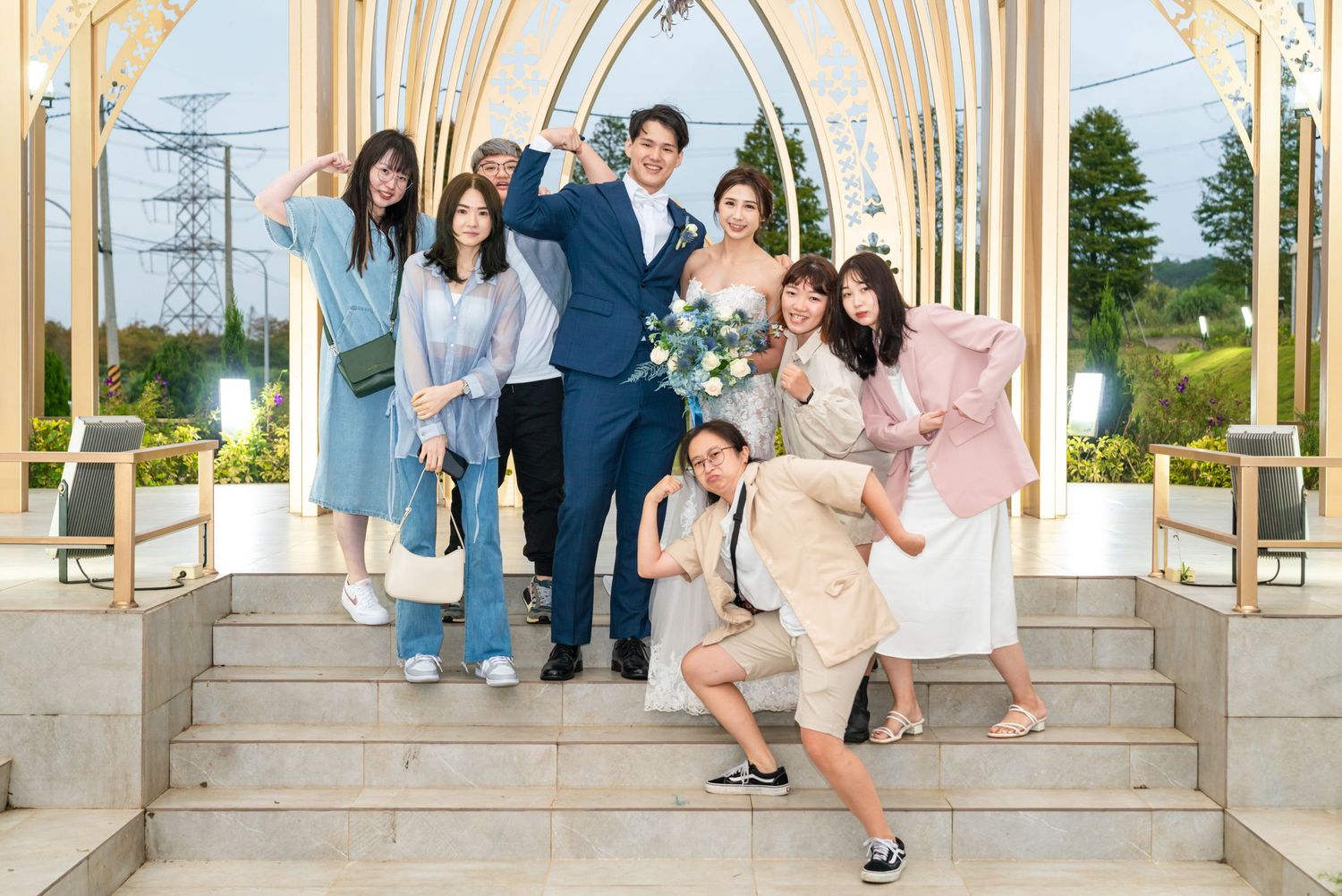 A group poses together on stone steps in front of an elegant white archway on a sunny day.