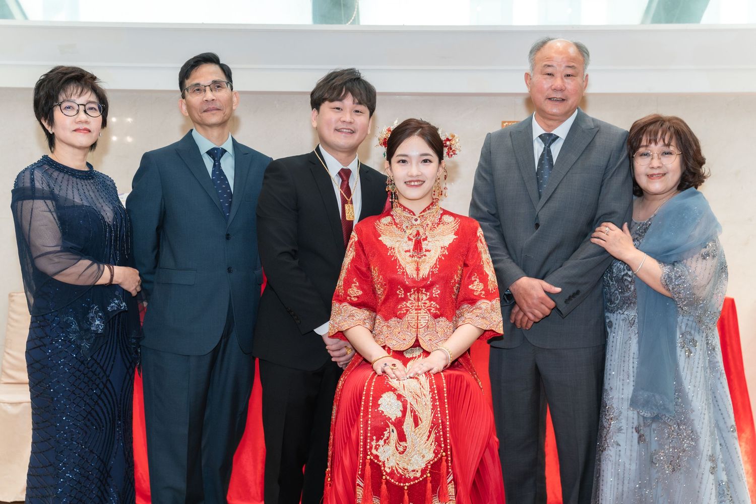 A group of formally dressed people at a traditional Chinese wedding celebration with the bride wearing a red qipao dress.