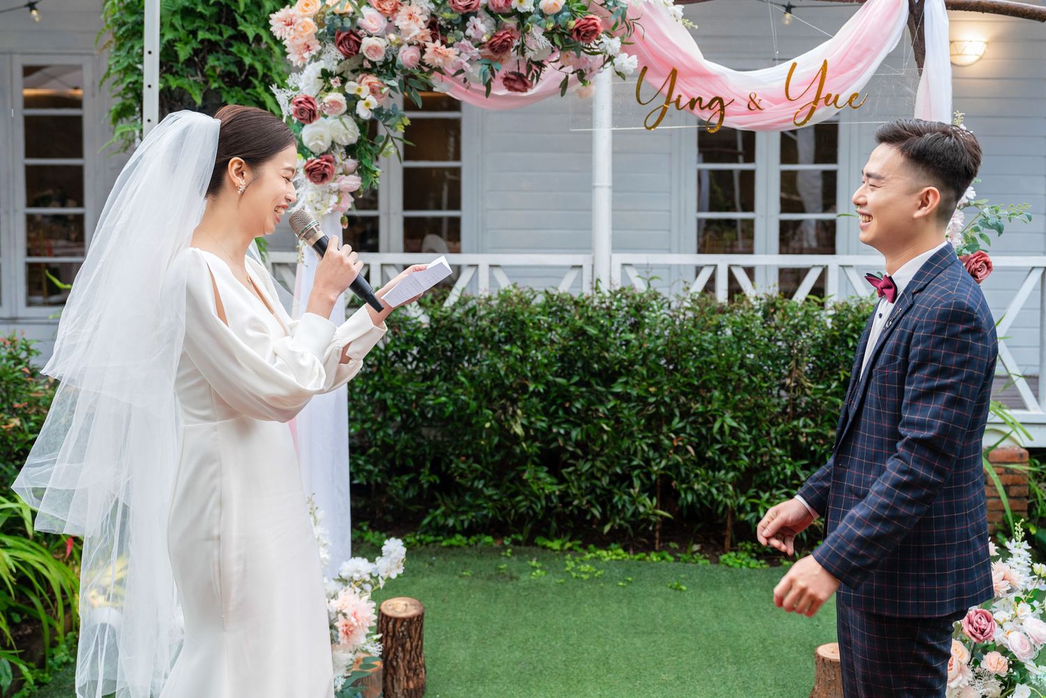 An outdoor garden wedding ceremony with floral decorations and two people exchanging vows under an arch.