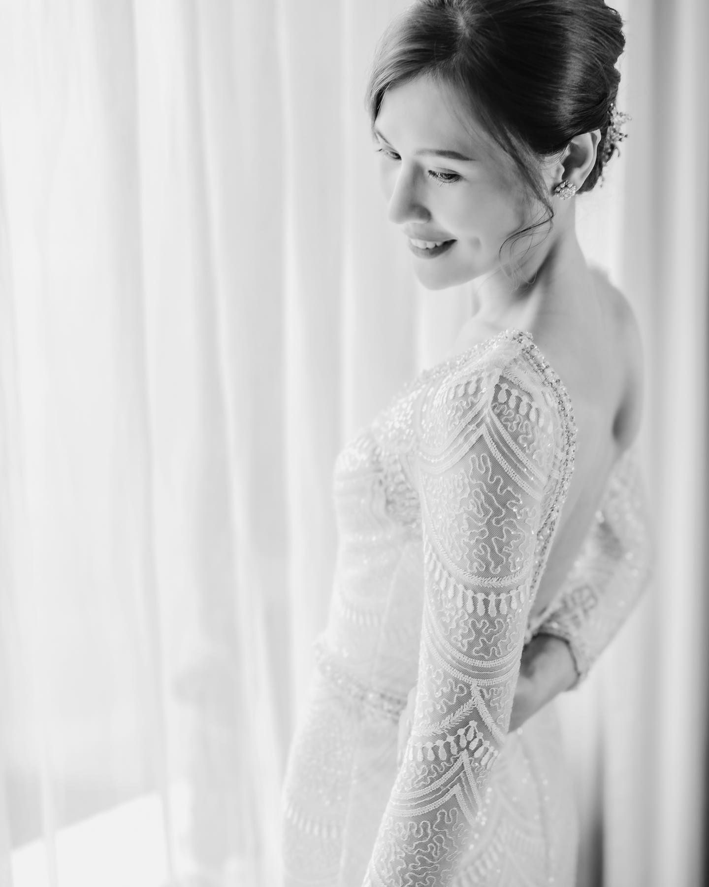 Black and white portrait of a bride in a long-sleeved lace wedding dress with geometric patterns.