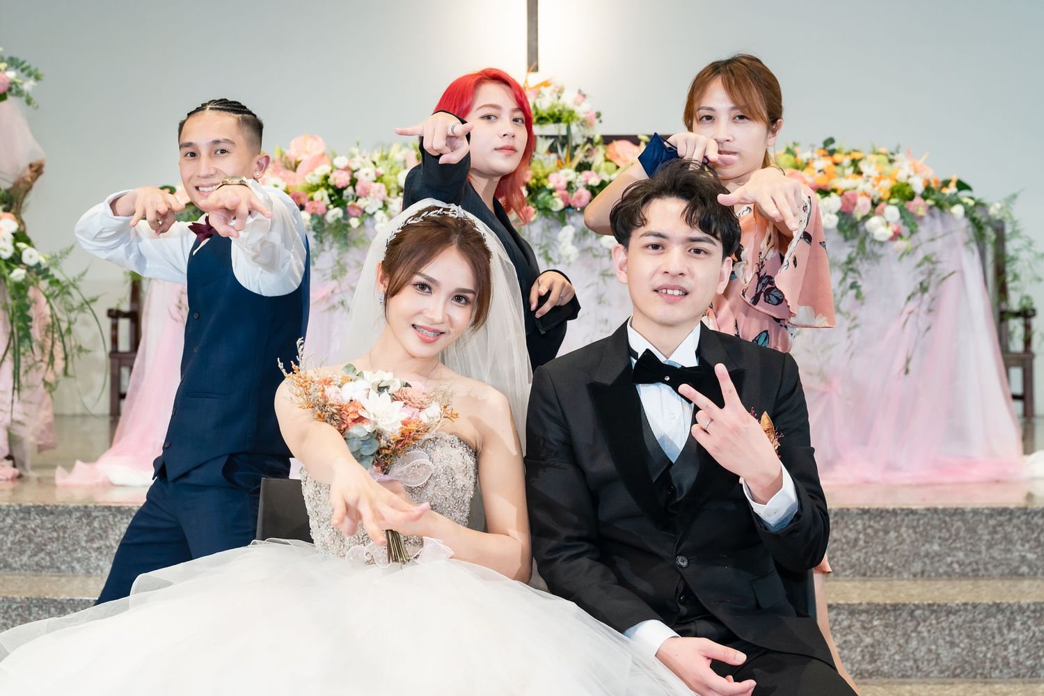Wedding party poses playfully on decorated church steps with floral arch backdrop.