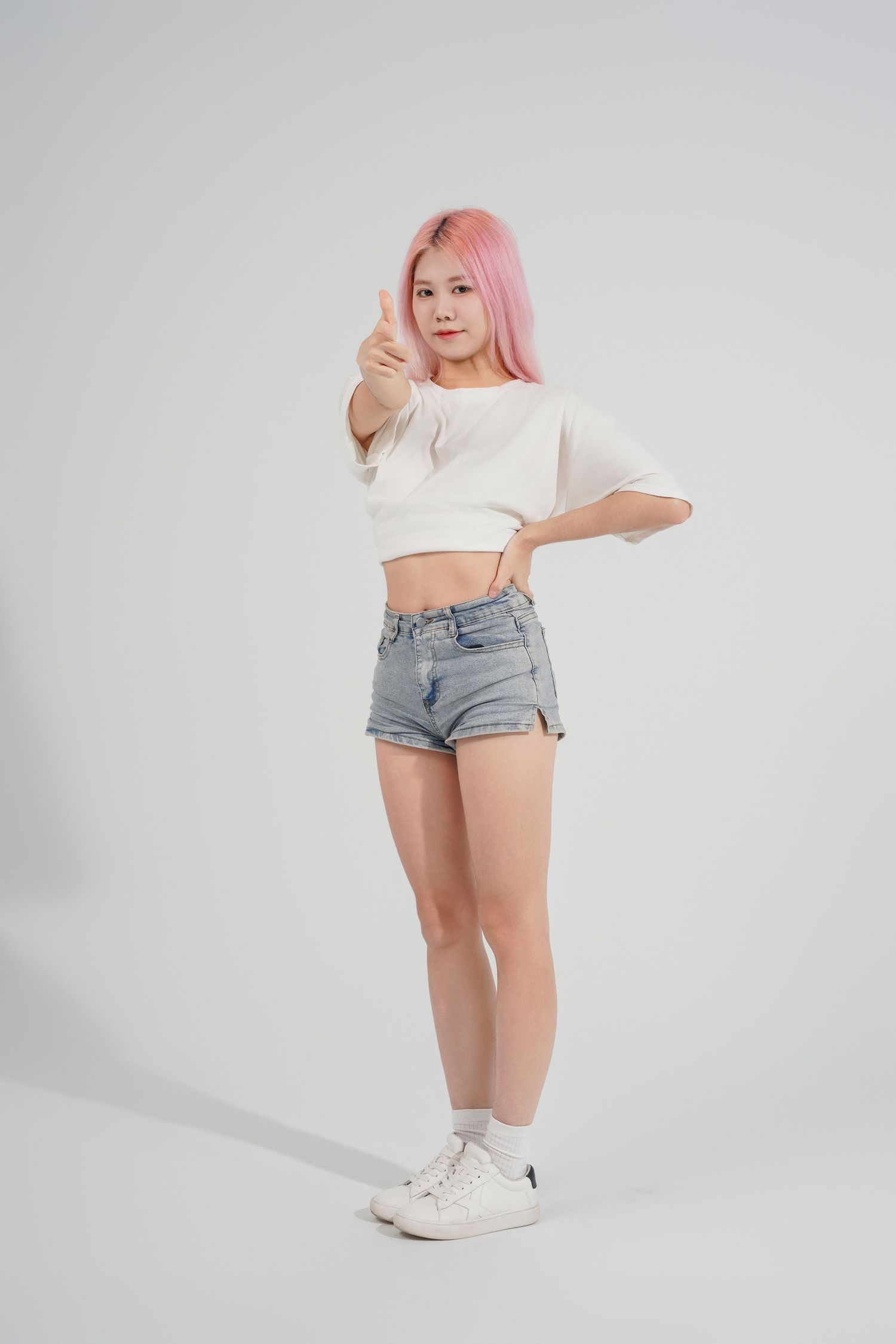 Model in denim shorts and white crop top with pink hair poses against white background in three different positions.