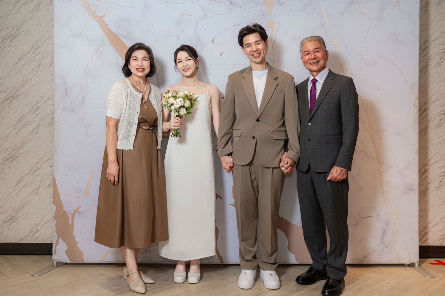 Four people pose together at a formal event, with the bride in white holding a floral bouquet.