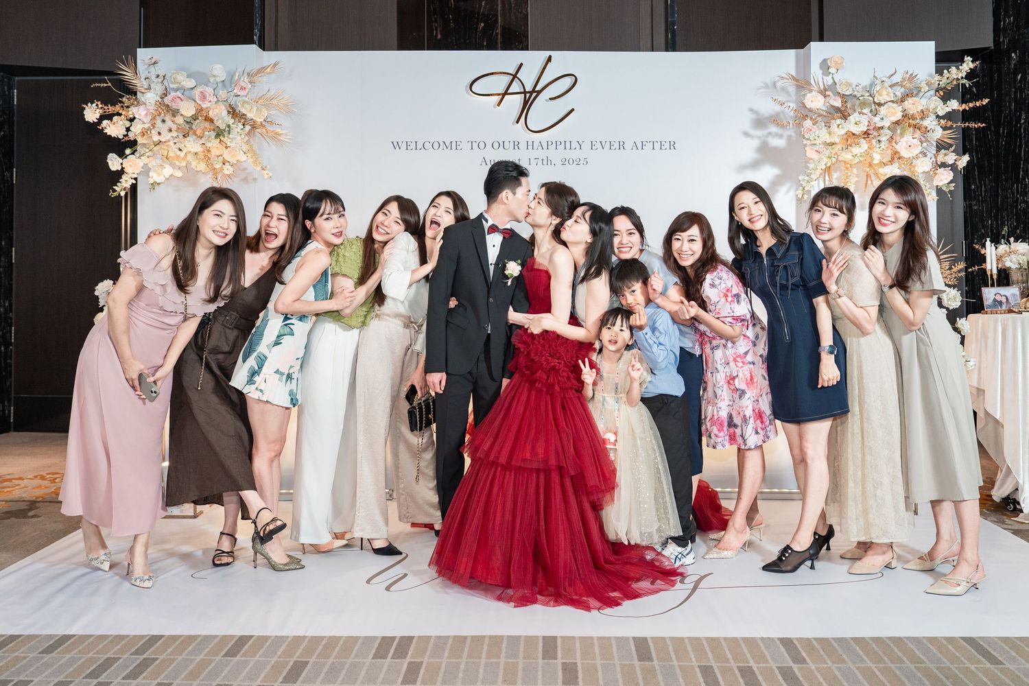 Wedding party members pose together in formal attire at an elegant reception venue with sparkling lights in background.