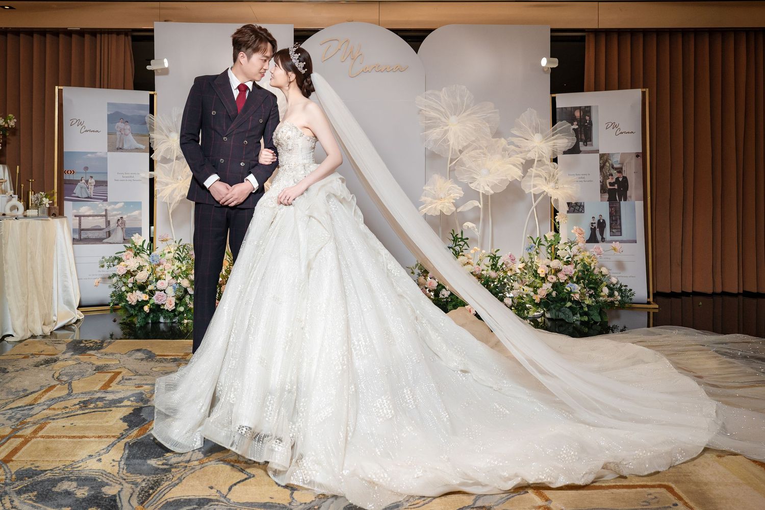 Elegant bride in white ball gown wedding dress shares a romantic kiss with groom in navy suit at decorated venue.