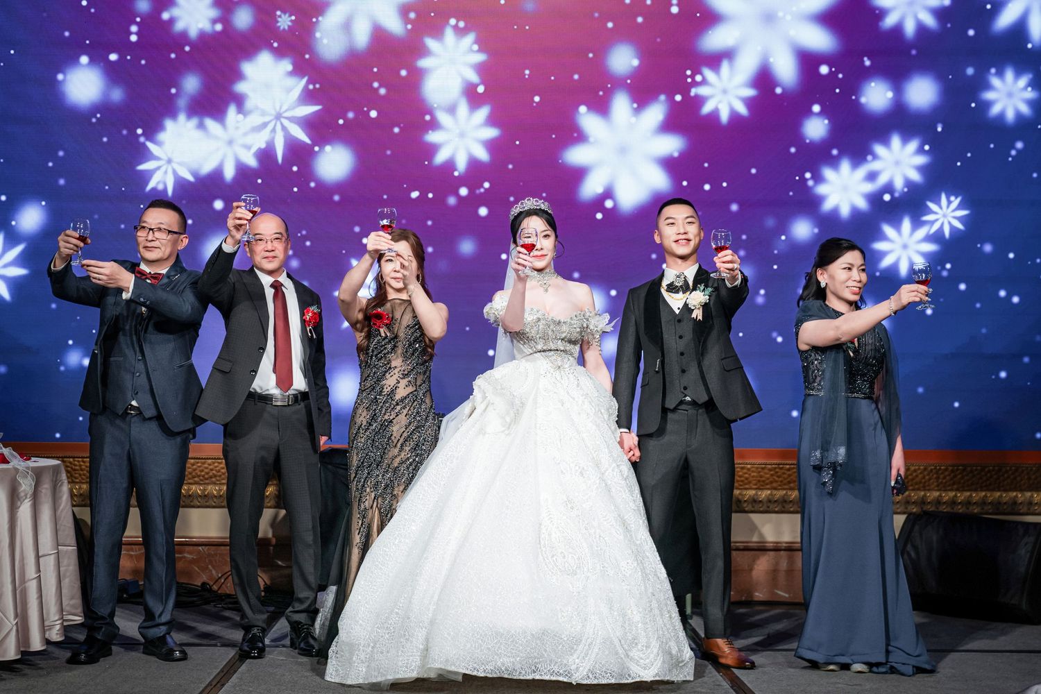 Wedding party poses together under glowing snowflake lights during an evening celebration.