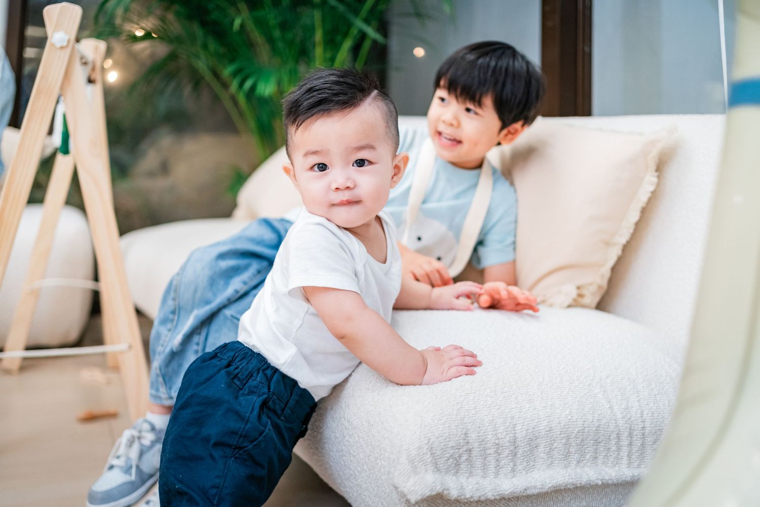 Baby in white sweater sits on cozy couch while playing with parent in natural light setting.