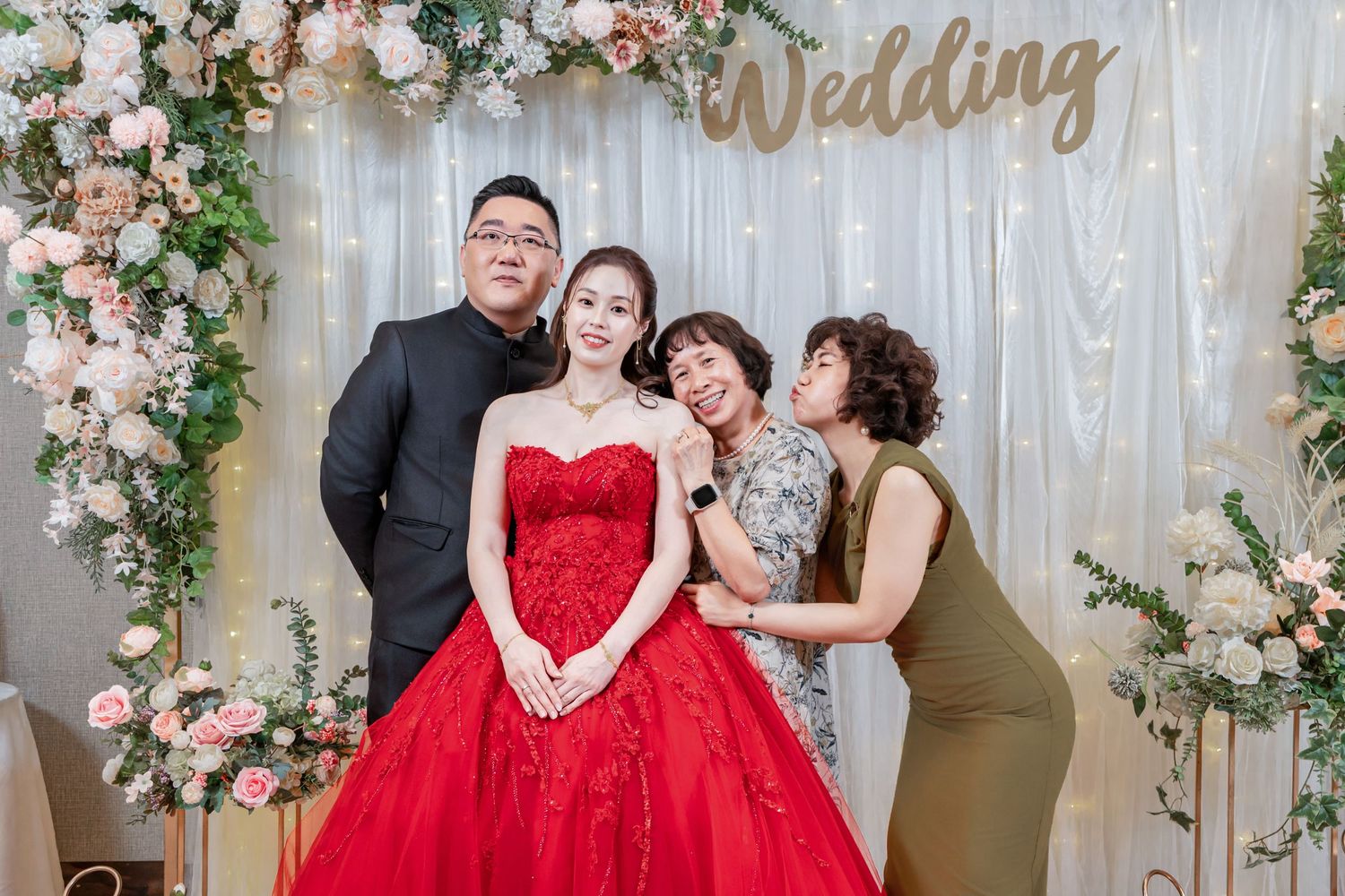 Wedding celebration with elegant floral arch decorations and guests in formal attire including a red gown.