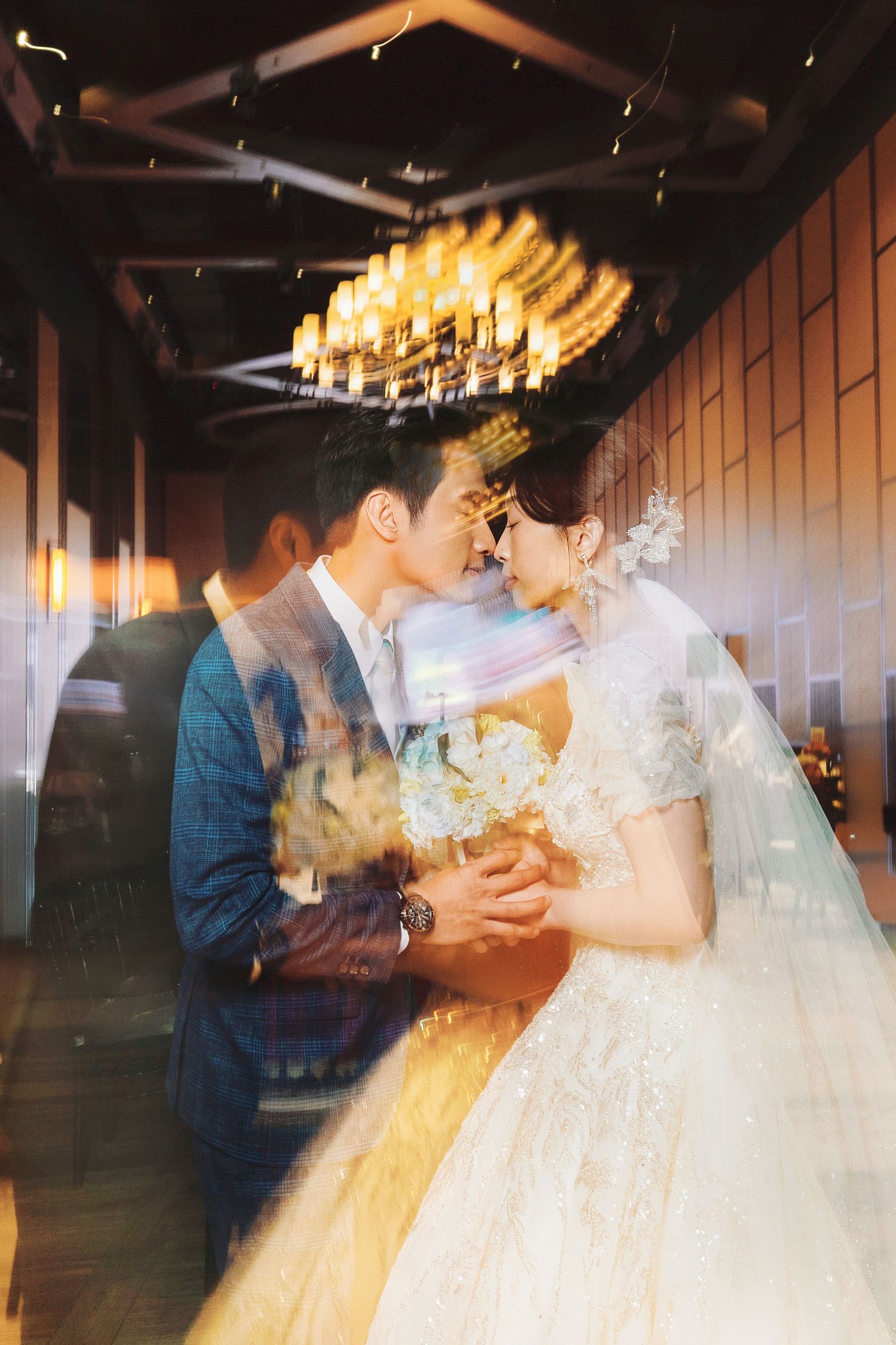 An intimate wedding moment captured in an elegant venue with a dramatic chandelier and warm lighting.
