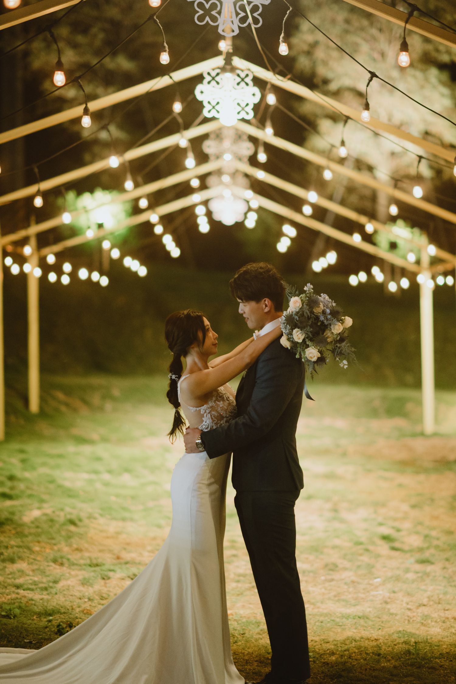A romantic wedding ceremony under a clear tent with glowing string lights creates a magical evening atmosphere.