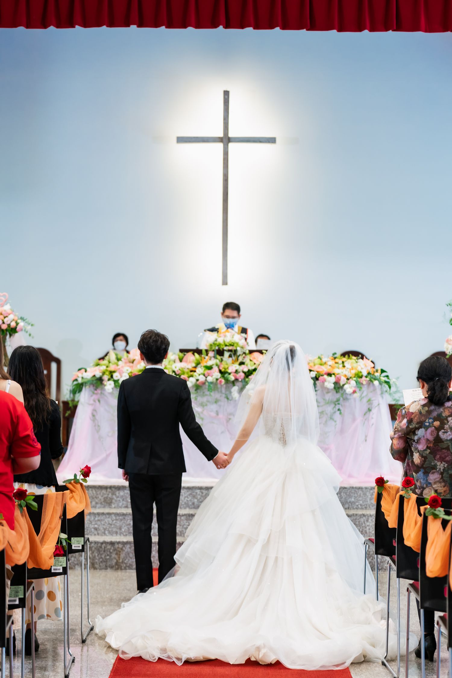 Church wedding ceremony with illuminated cross and floral arrangements at the altar.