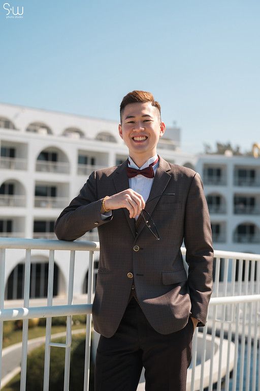 Groom in classic brown suit and bowtie poses on hotel balcony.