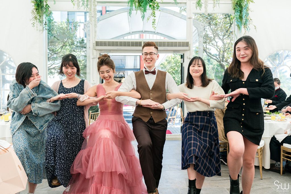 Group performs choreographed dance moves at wedding reception with someone in a pink gown.
