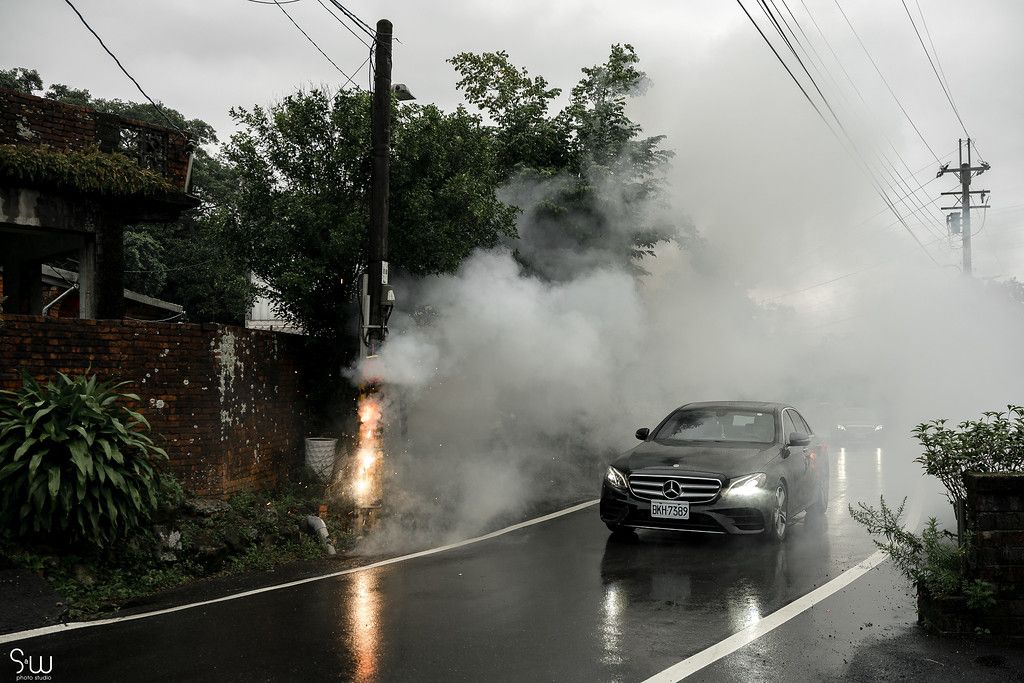 Car driving through heavy smoke and rain on a misty mountain road.