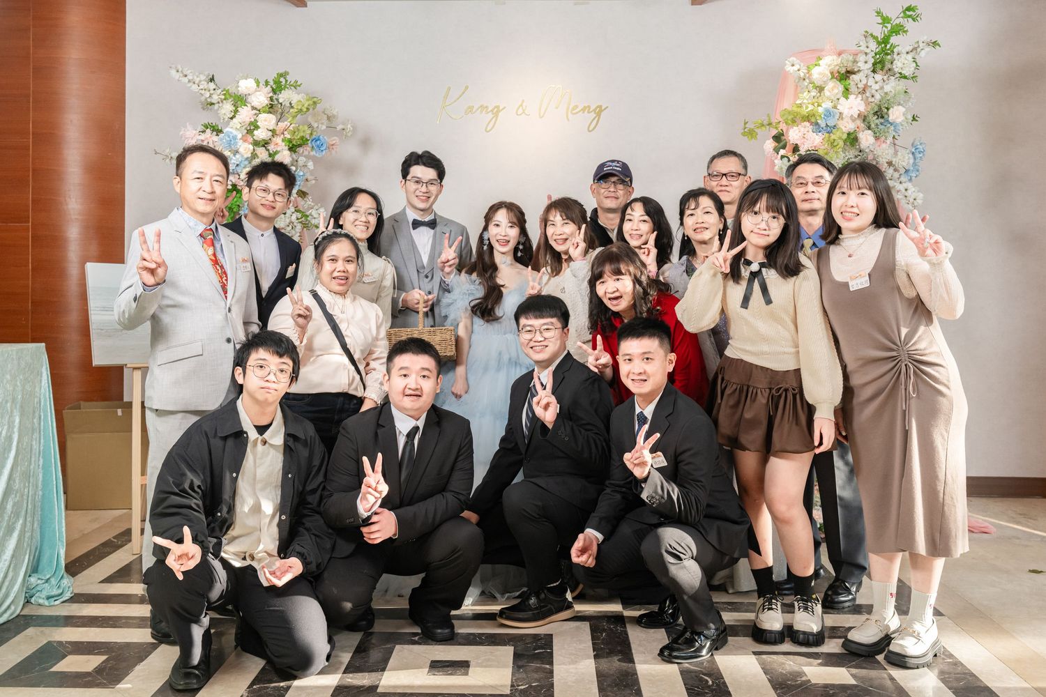 A group of wedding guests and attendees pose together for a formal photo in an elegant indoor venue.