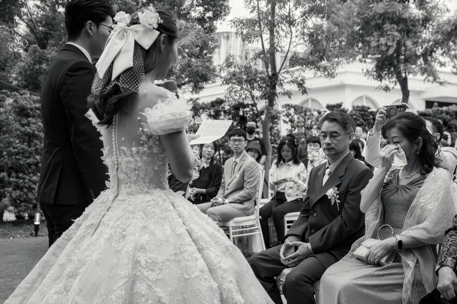 A couple shares a joyful moment during their outdoor wedding ceremony while surrounded by guests and trees.