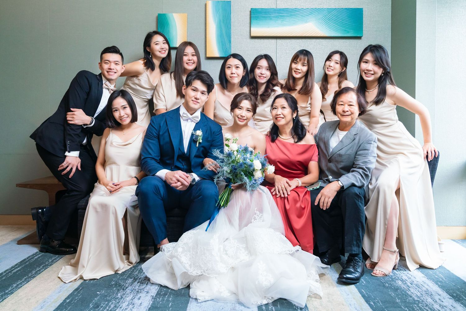 A wedding party poses together on a plush gray carpet in front of a turquoise accent wall.