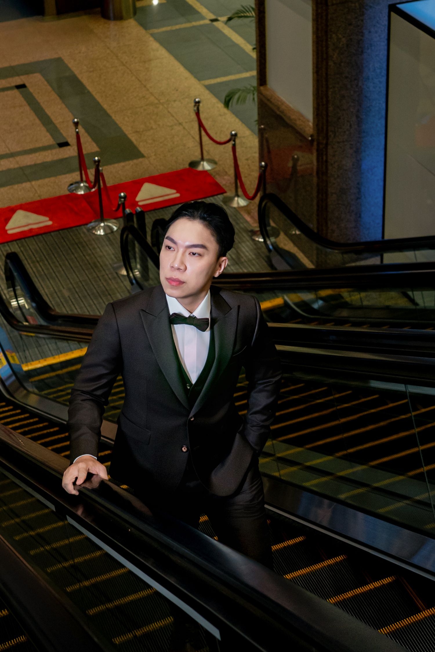 A person in a dark suit and red baseball cap sits on stairs in an indoor parking garage.