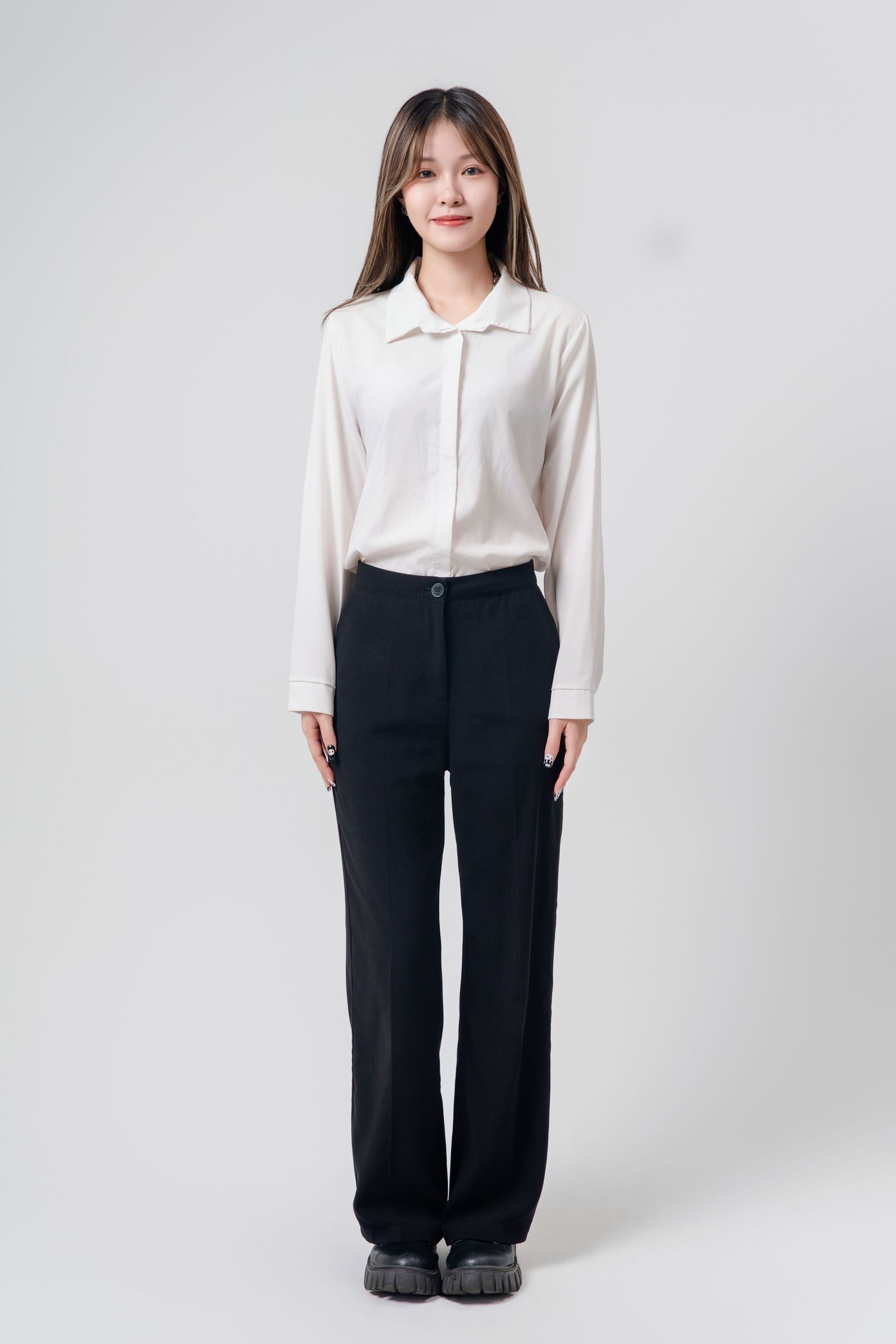 A person wearing a classic white button-down shirt and black wide-leg trousers stands against a light gray background.
