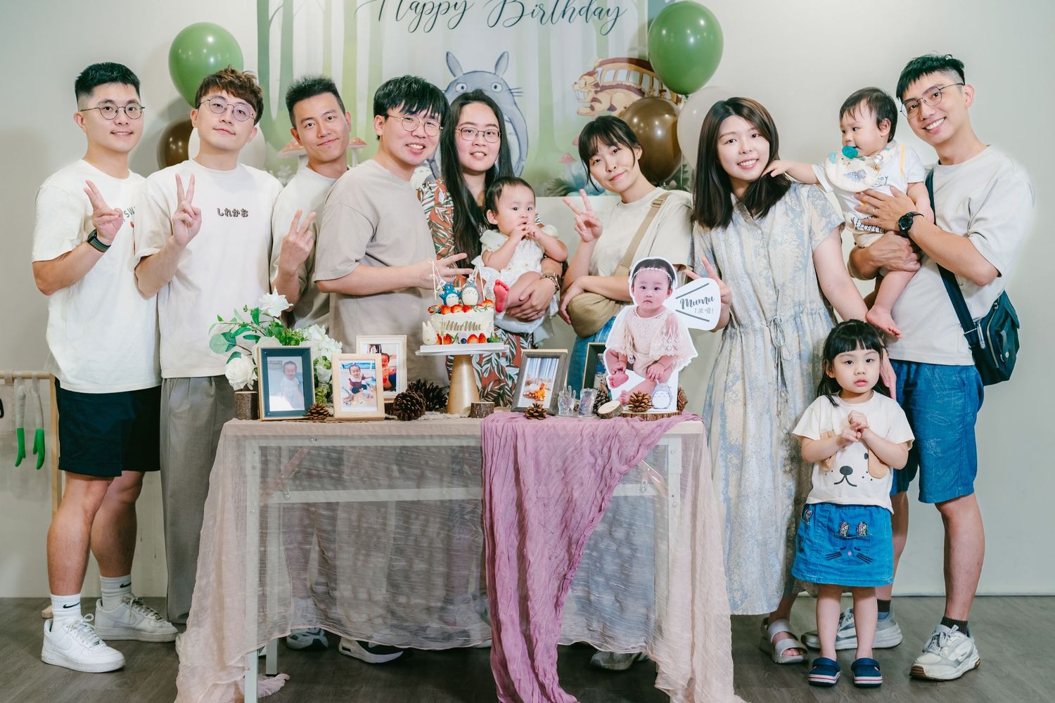 A birthday party gathering with green balloons, dessert table and partygoers posing together for a celebration photo.