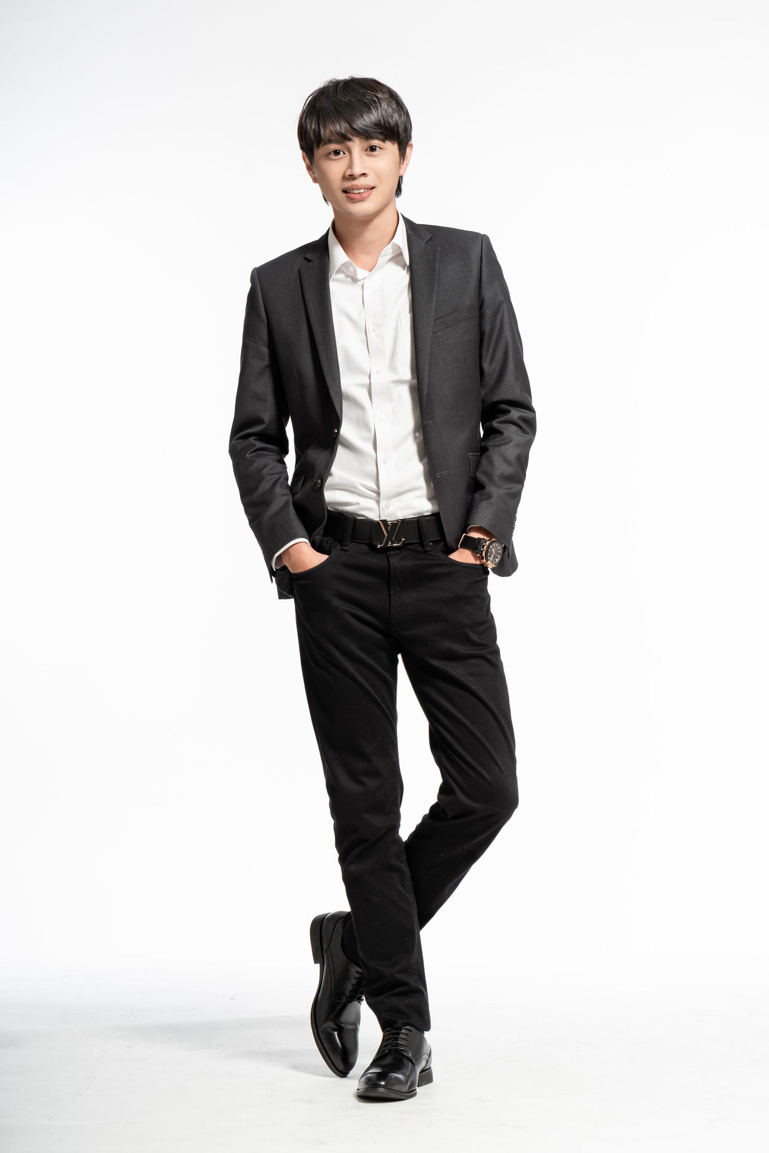 Professional portrait of a person in formal business attire with black suit jacket, white shirt and dress pants against white background.