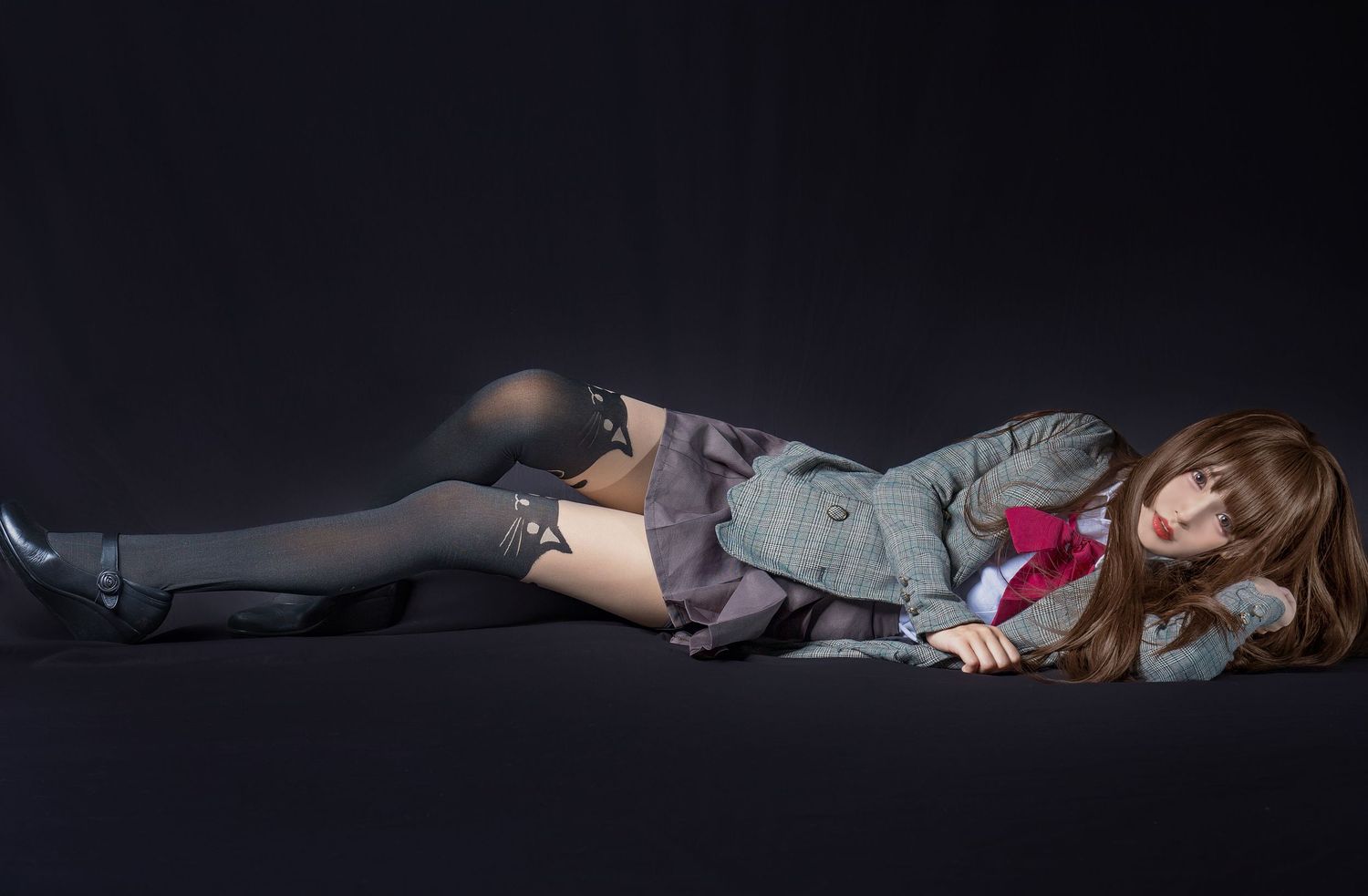 Figure lying on dark floor in gray stockings, shorts and jacket with red accents against black background.
