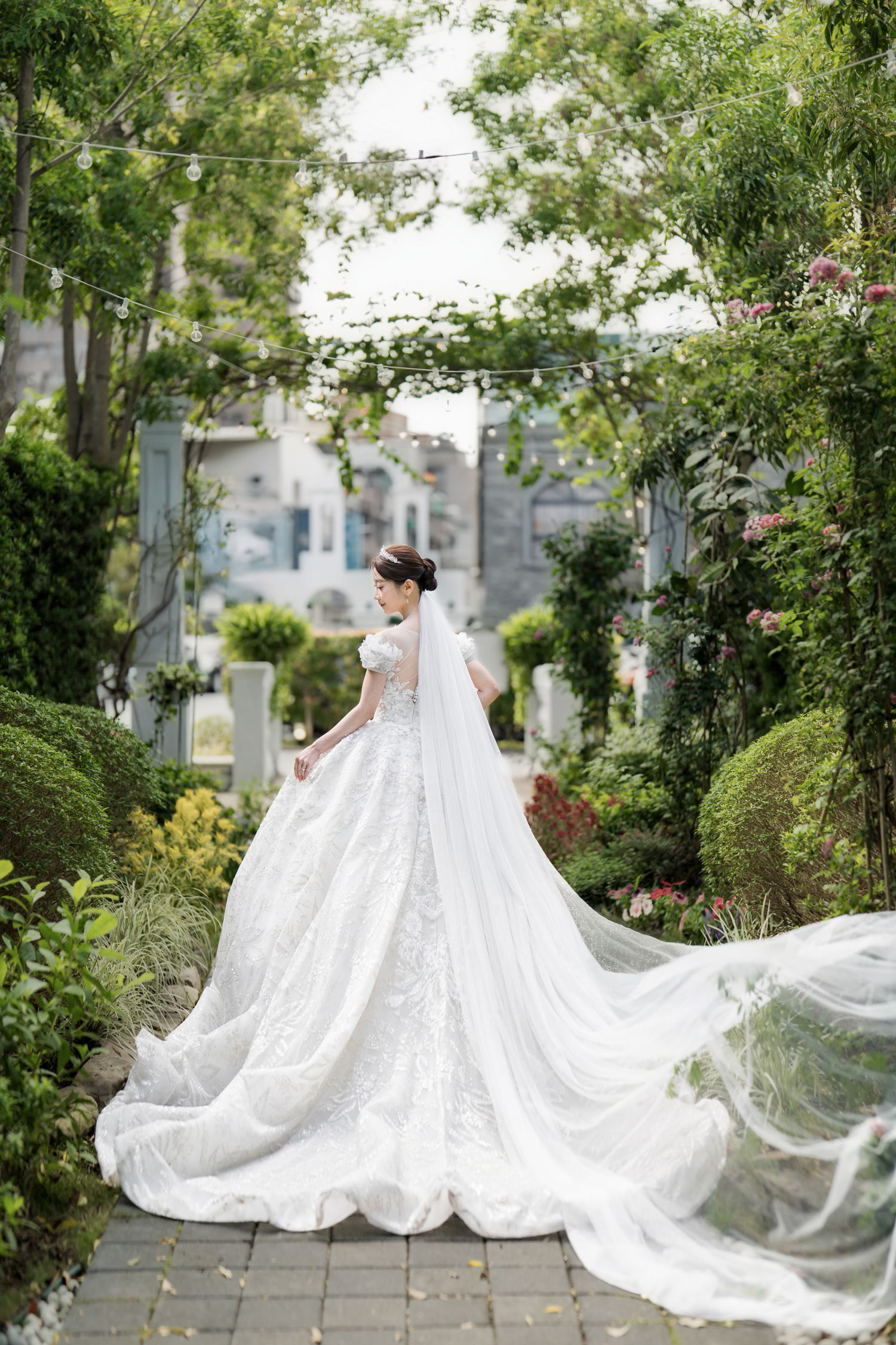 A flowing white wedding dress with a dramatic cathedral-length veil captured in a lush garden setting.