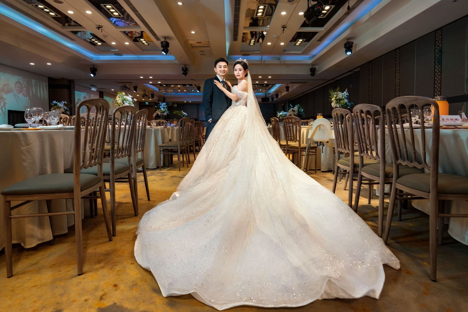 Elegant white wedding dress with flowing train displayed in luxurious reception venue with modern lighting and decor.