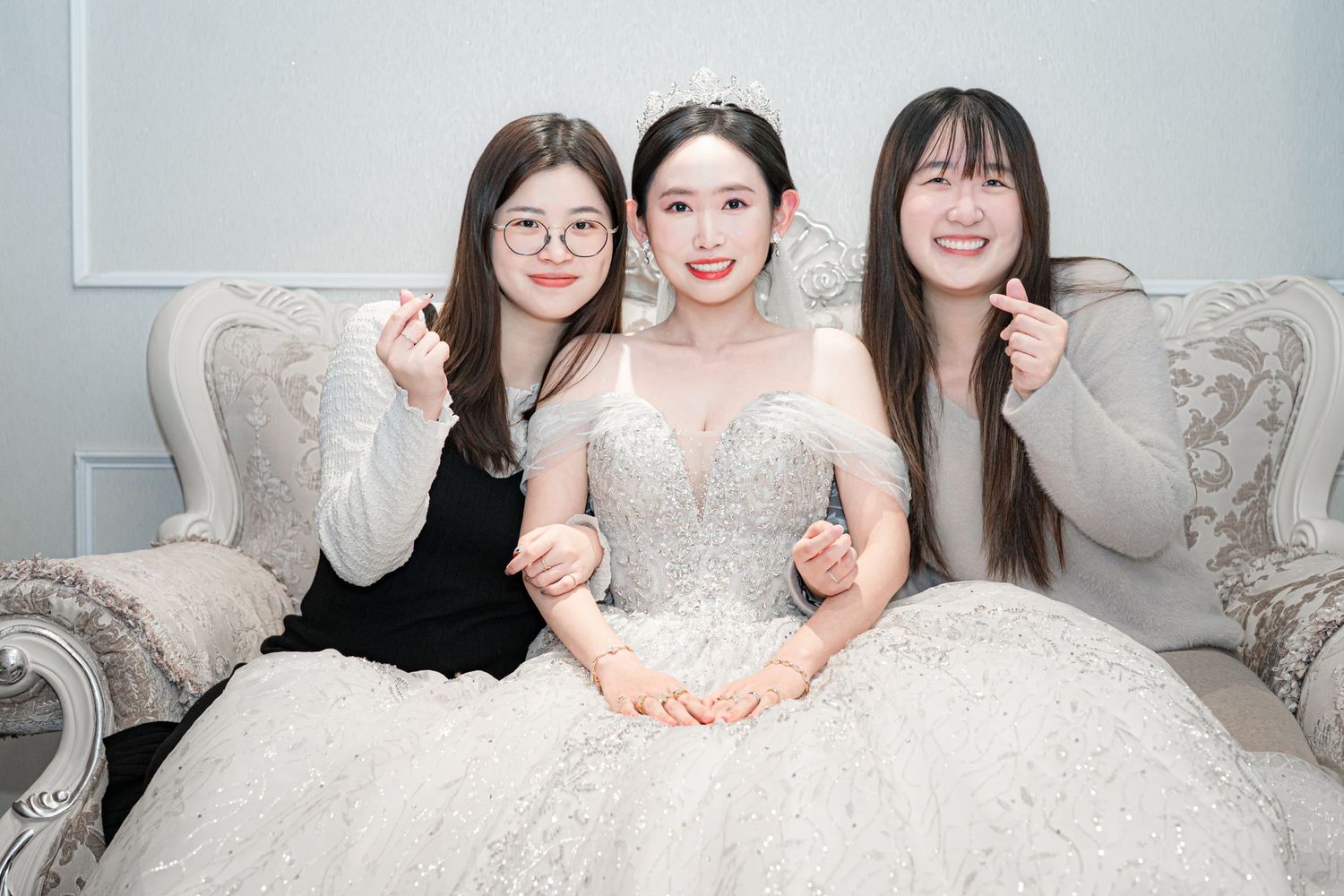 A group in white dresses pose together on a light gray couch during what appears to be a bridal event.