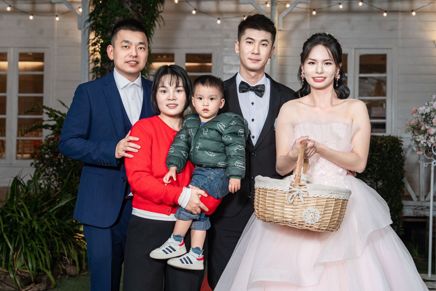 A formal family portrait at an elegant event with string lights and greenery in the background.