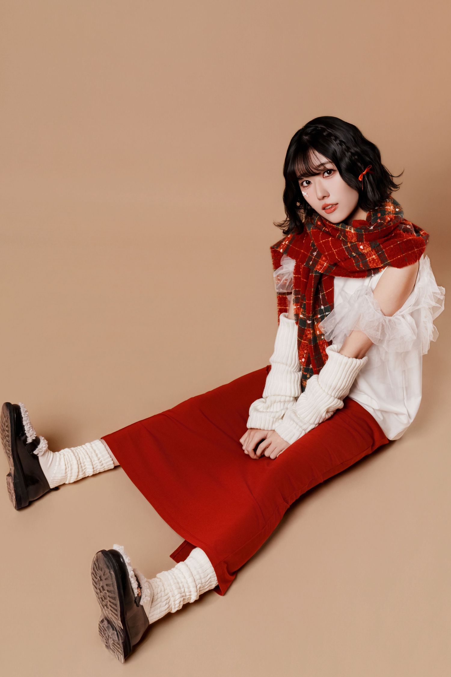 Fashion model poses in white blouse and red dress against beige backdrop in artistic photo series.