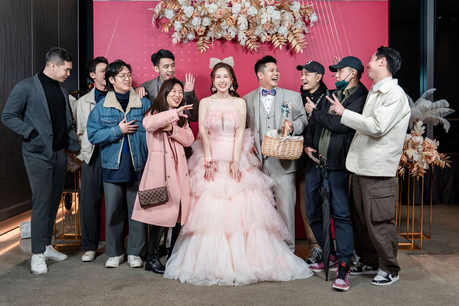 Wedding guests gather at a reception venue with pink decor and a crystal chandelier overhead.
