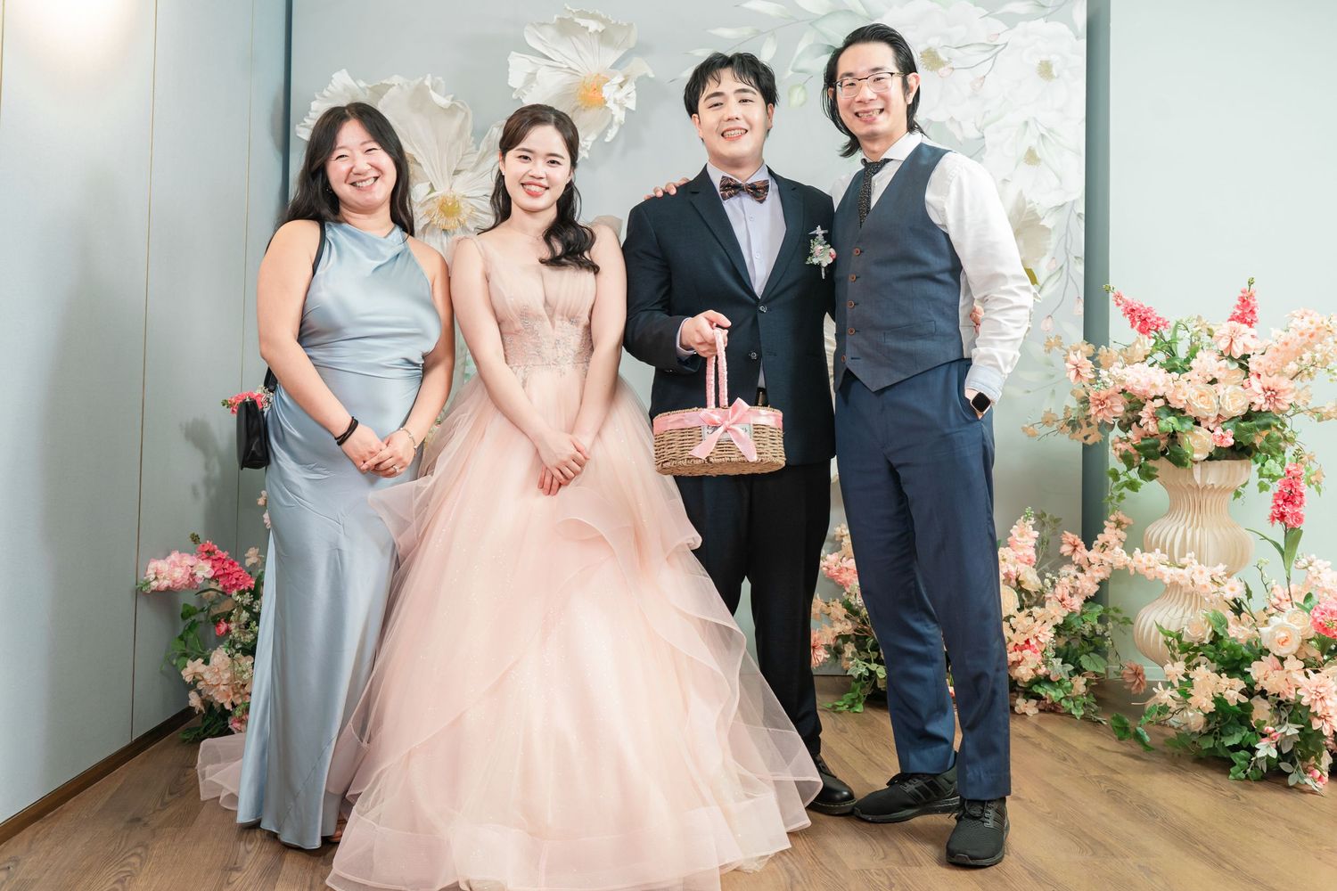 A wedding celebration scene with people in formal attire and pink floral decorations in the background.