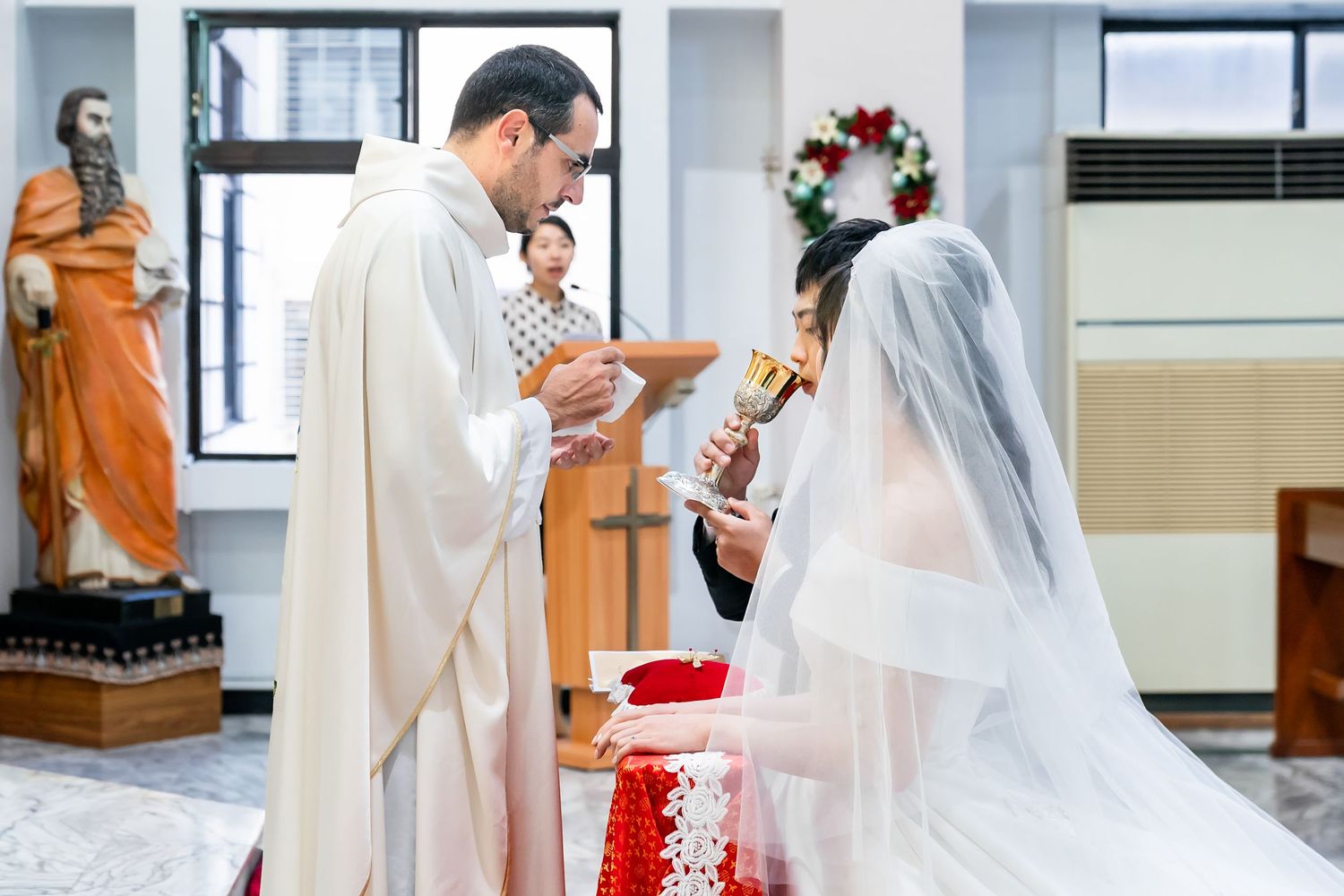 Priests conducting communion ceremony at traditional Catholic wedding mass with decorated altar.