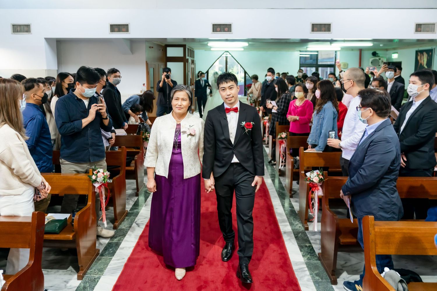 Wedding ceremony processional with couple walking down red-carpeted church aisle.
