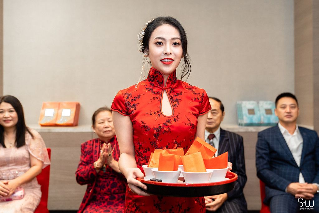 Someone in a red qipao dress serves tea during a traditional Chinese wedding ceremony.