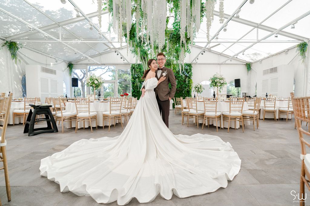 A stunning wedding reception venue with a dramatic cathedral-length white dress against hanging greenery decor.