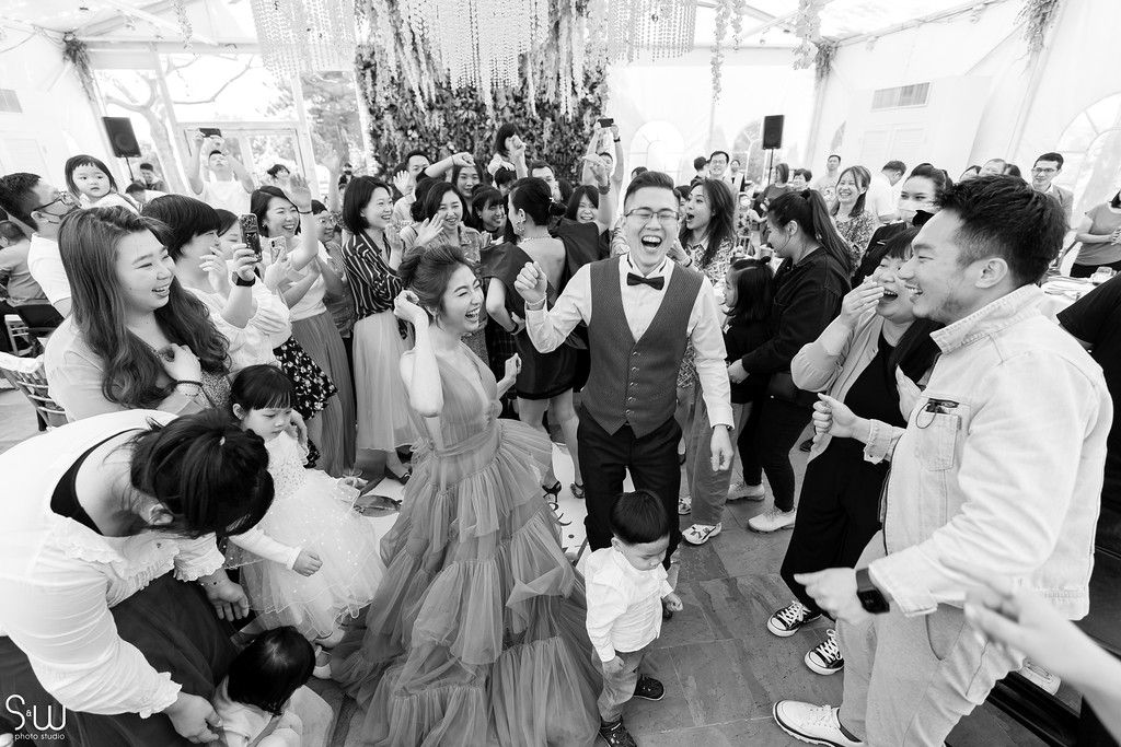 A black and white shot of wedding guests dancing and celebrating on a crowded dance floor.
