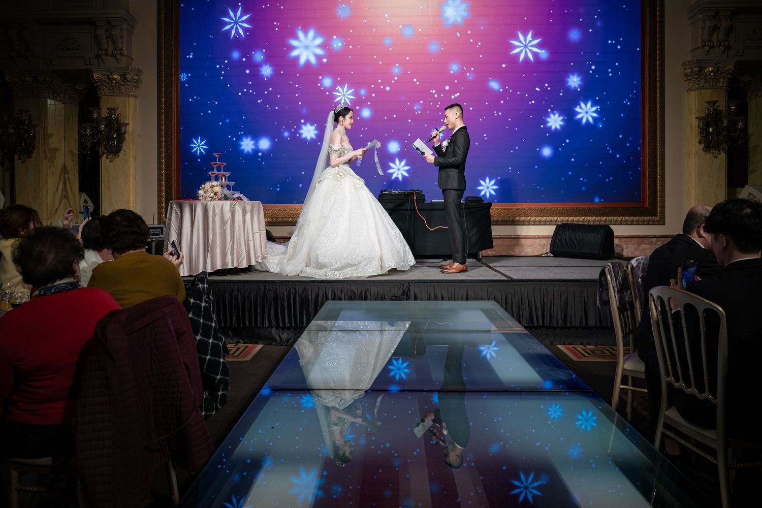 A fashion show runway illuminated with blue lights and snowflake projections showcasing elegant formal wear.