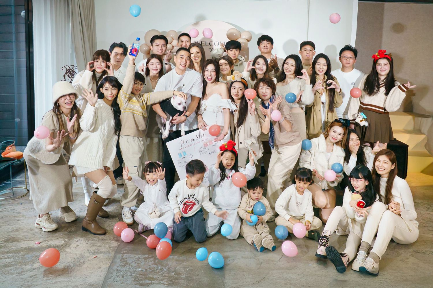 Large group of people posing together with pink and blue balloons in a bright indoor space.