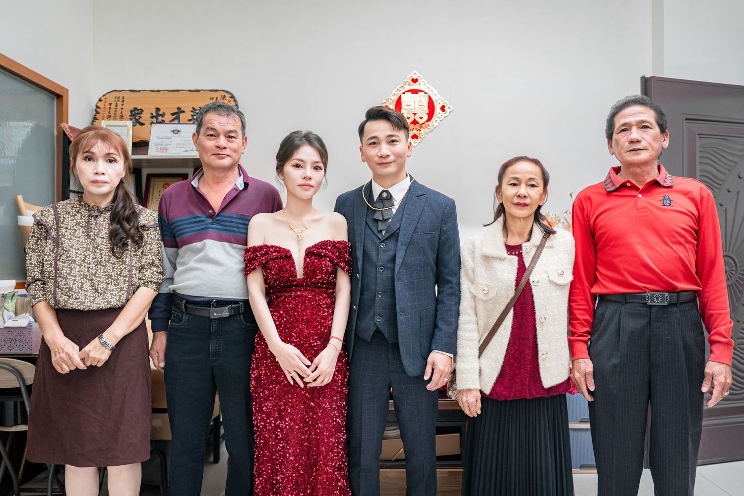 A group of people wearing formal attire including red dresses and dark suits pose together at an event.