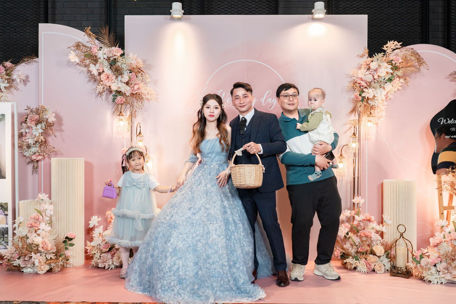 Wedding party members in light blue dresses and black tuxedos celebrate during an elegant pink-themed reception.