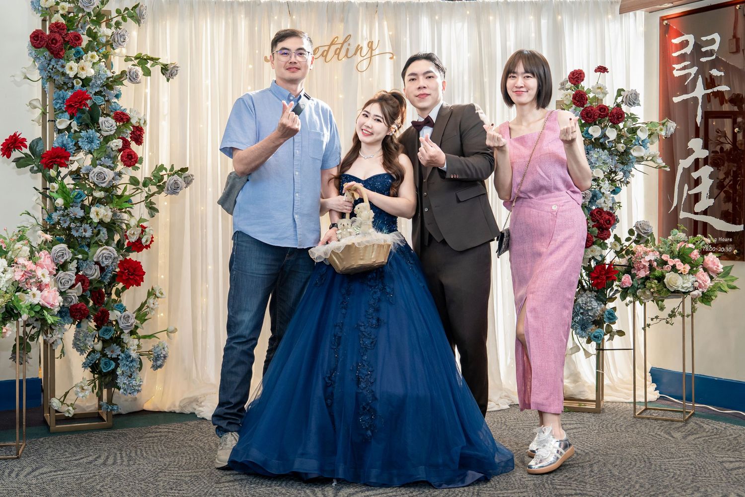A group poses together at a celebration event with red floral decorations and a person wearing a blue ballgown.
