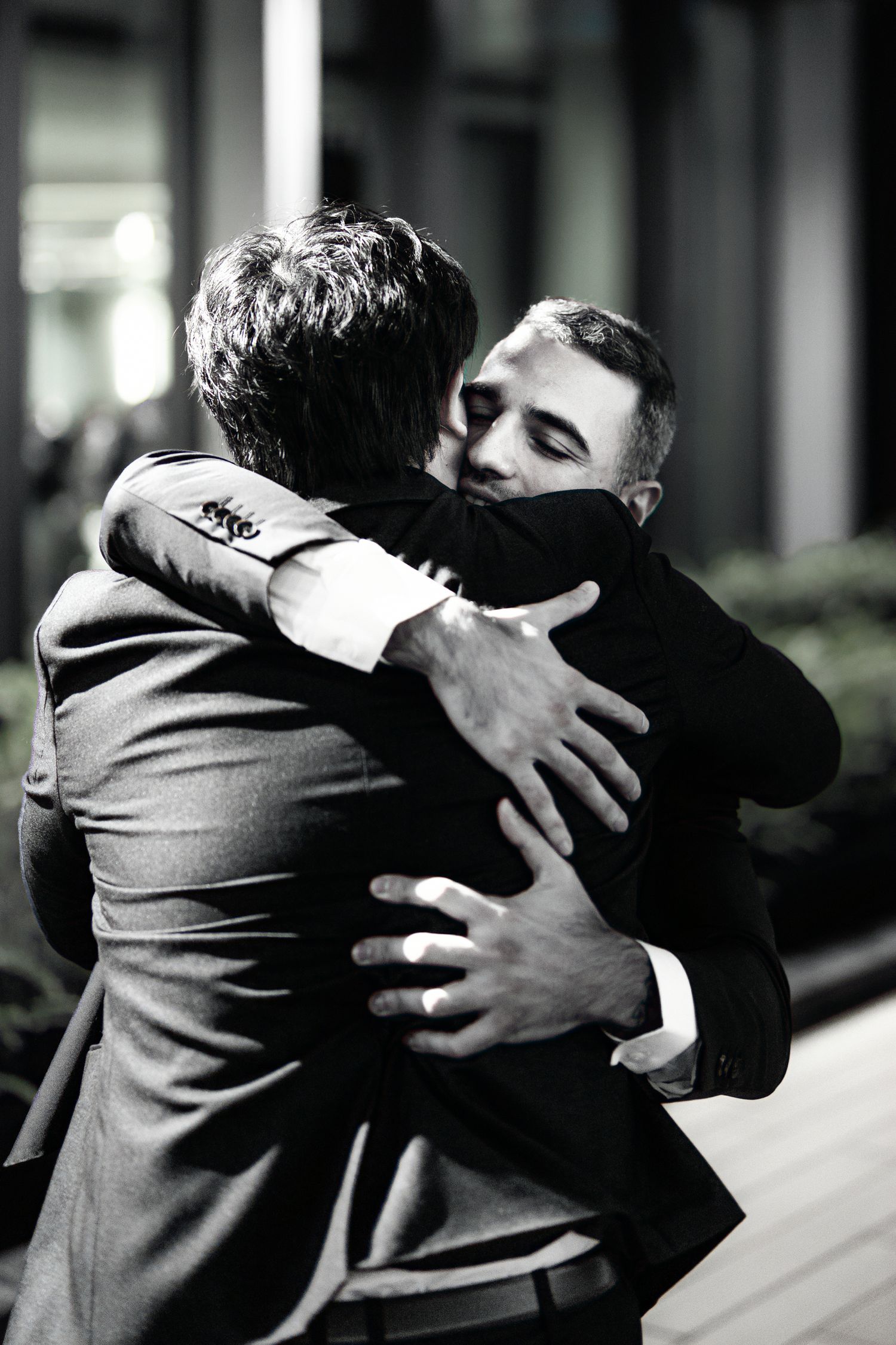 Two people in formal attire share an emotional embrace in black and white photography.