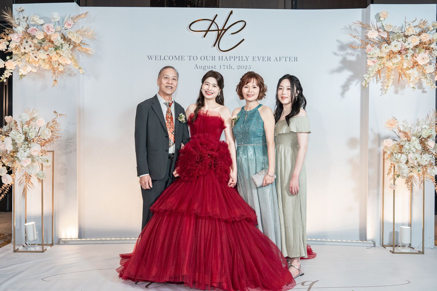 Wedding party poses in formal attire with the bride in a stunning deep red gown and others in sage green dresses.