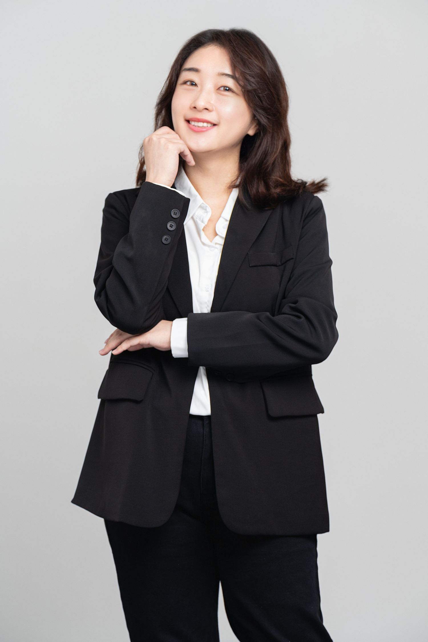 Professional in a black business suit with white blouse poses confidently against a gray background.