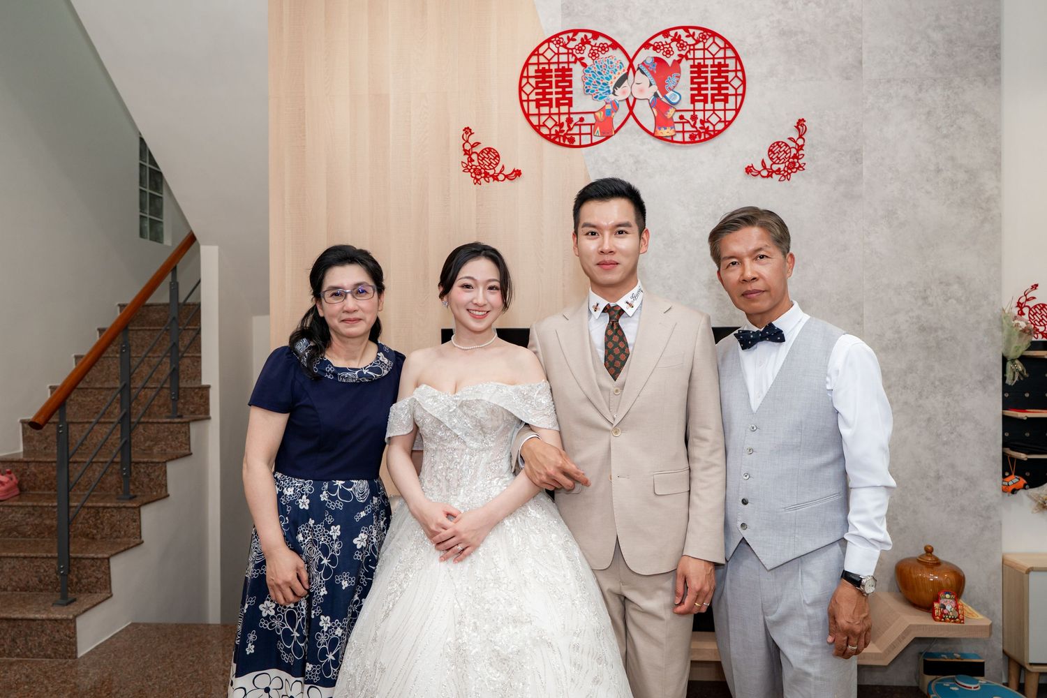 A bride in a white gown poses with groom in beige suit and two family members at a traditional Chinese wedding.