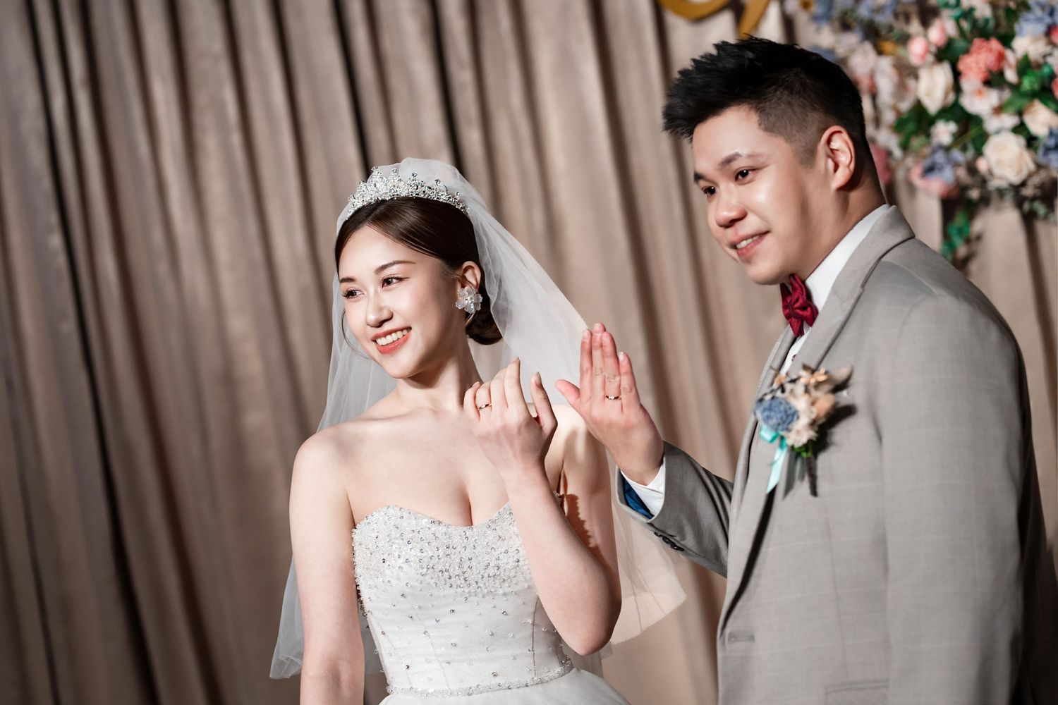 A happy couple shares joyful moments during their wedding celebration with grey and floral decor in the background.