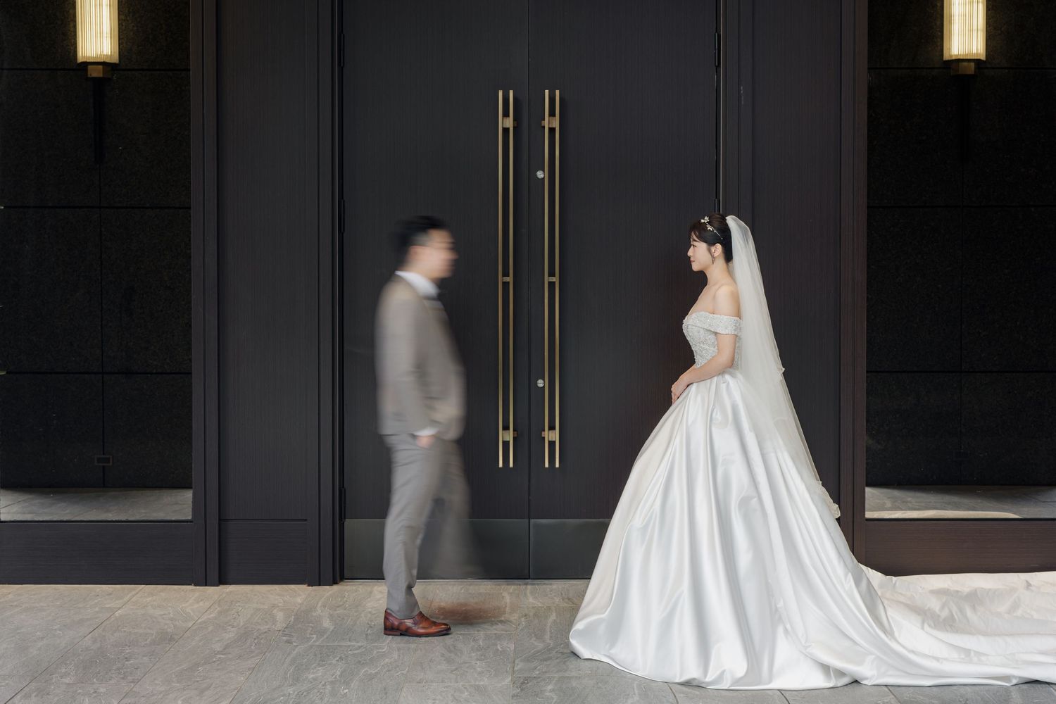 A wedding couple walks down an elegant dark hallway with illuminated wall sconces and gold accents.